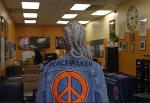 Erica's back facing the camera with a jean jacket that has an orange peace sign on it and the text 'peacemaker'