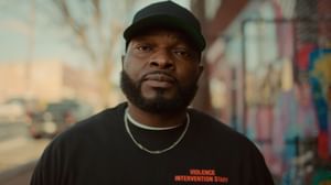 Black male with shirt that says volence intervention staff speaking towards the camera outside