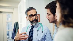 Medical professional using his hand as he speaks to two adults looking at him