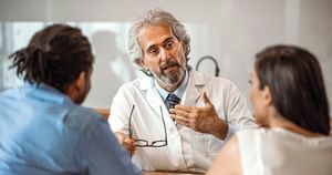 Backs of two parents to the left and right of a doctor speaking towards them