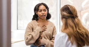 Young female patient with hand on chest as she speaks to female doctor