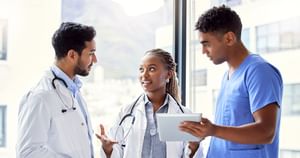 Female and 2 male health care professionals talking and standing ifront of a window