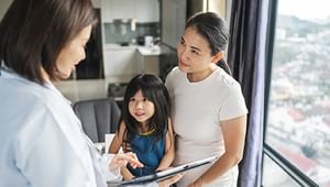 Mother with daughter on her lap smiling at female doctor speaking to them