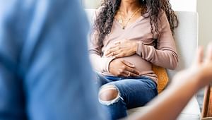 Close up of the back of a shoulder of a medical professional with pregnant woman holding her stomach across from her sitting down