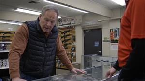 White gentleman leaning over the counter looking at the gun selection at a gun shop