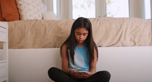 Young girl sitting in her room against her bed on the floor looking at her phone