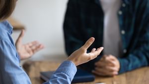 Close up of expressive hands with an individual in the background with their hands crossed listening.