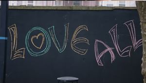 "love all" written in colorful chalk on a black brick wall outside